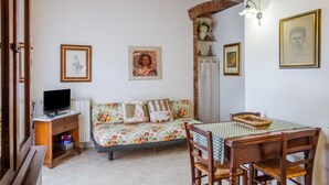 Ein gemütliches Wohnzimmer mit einer Couch, einem Fernseher, einem Esstisch mit Stühlen und gerahmten Bildern an den Wänden.