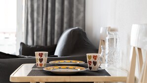 Una bandeja con platos, vasos y una jarrón sobre una mesa en una habitación con un sofá gris y cortinas.