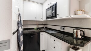 Una cocina con armarios blancos, encimera negra, microondas, hervidor y tostadora.