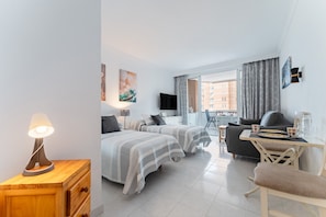 A hotel room with two beds, a desk, a chair, a lamp, and a TV.