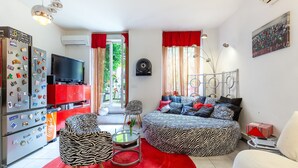 Een moderne woonkamer met een flatscreen televisie, rode kasten, een stoel met luipaardprint en een rond bed met een zebraprint dekbed, en een rood vloerkleed.