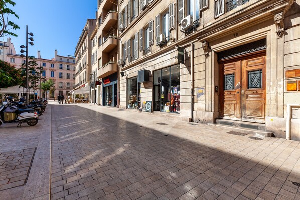 Une rue bordée d’immeubles, avec un trottoir pavé et des scooters garés.