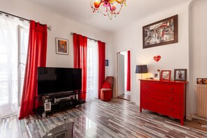 Un salon moderne avec un téléviseur à écran plat, des rideaux rouges, une commode rouge et un lustre.