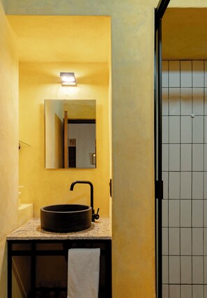 A bathroom with a round sink, a mirror, and a tiled shower area.