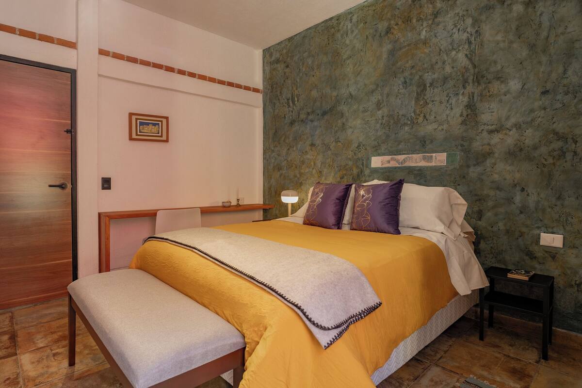 Ein Schlafzimmer mit Bett, Sitzbank, Nachttisch und einer Wand mit Struktur.