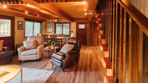 A spacious living area with a wooden staircase, leather armchairs, and a dining table.