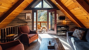A cozy attic room with wooden beams, a large window, and a view of the outdoors.