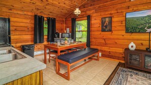 A wooden cabin interior with a kitchen, dining area, and a large window with a view of greenery. - Denton Go Cabin #3 | Denton Hill State Park (Ulysses)