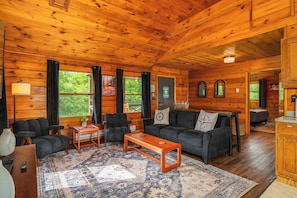 A wooden cabin interior with a sofa, chairs, a coffee table, and a rug.