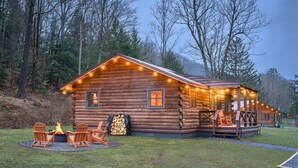 A log cabin with a fire pit and outdoor seating, surrounded by trees.