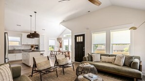 A spacious living area with a sofa, chairs, and a coffee table. There is a kitchen in the background with a dining table. - Wave Haven - Bali Style! Hot Tub! Near Bay & Beach (Kill Devil Hills)