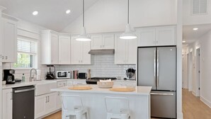Une cuisine moderne avec des meubles blancs, un réfrigérateur en acier inoxydable et un îlot central doté de tabourets.