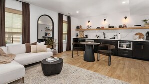 A modern living room with a sofa, coffee table, and a dining area with chairs. - Cocoa Capri - Luxury Getaway (Kill Devil Hills)