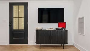 A room with a black door, a black cabinet with a red box, and a mounted TV on the wall. - Cocoa Capri - Luxury Getaway (Kill Devil Hills)