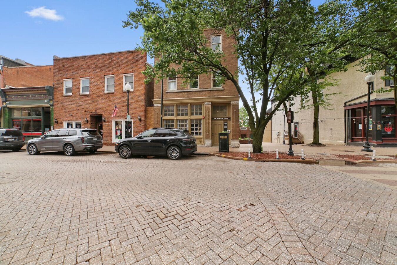 A paved street with brick buildings, parked cars, and trees.