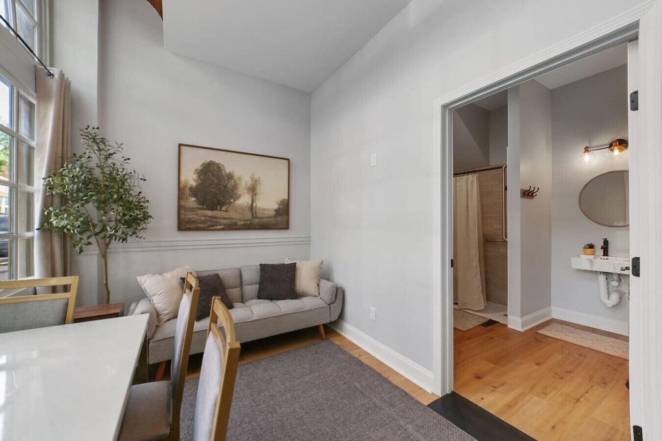 Une pièce comprenant un canapé, un tableau, une plante et une porte donnant sur une salle de bain.
