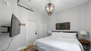 Un dormitorio con cama, televisor montado en la pared, puerta y lámpara.