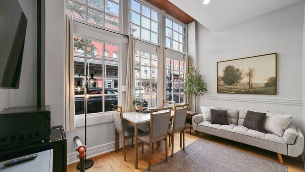 Una habitación con una mesa de comedor, sillas, un sofá, un cuadro y una ventana con vistas a edificios y coches.