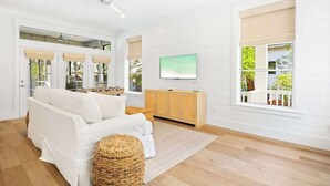 A modern living room with a sofa, a television, and a large window with a view of greenery.