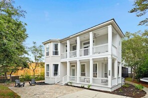 A two-story white building with a balcony on the second floor, a front porch, and a paved patio area with two chairs. - Pearly White by Stay on 30a (Seacrest)