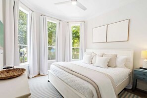 A bedroom with a large bed, a ceiling fan, and a view of greenery outside. - Pearly White by Stay on 30a (Seacrest)