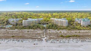 A resort with multiple buildings, a sandy beach, and a forested area in the background.