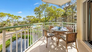 A balcony with wicker furniture, a table with blue and white plates, and a view of a river and trees.