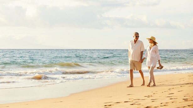 A couple walking on a sandy beach with the ocean in the background.
