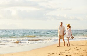 A couple walking on a sandy beach with the ocean in the background.