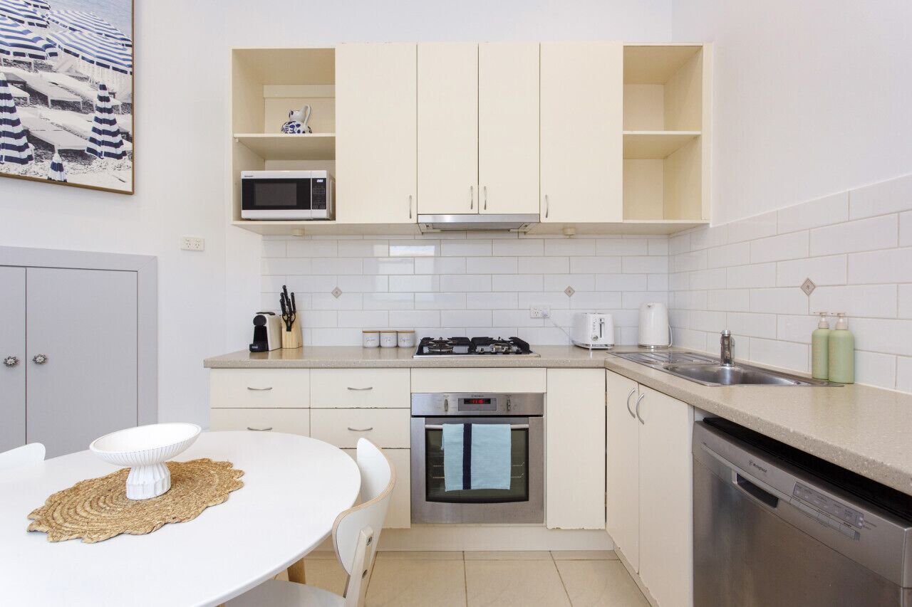 Une cuisine de taille réduite, avec des meubles blancs, un four à micro-ondes, une cuisinière, un four et un lave-vaisselle.