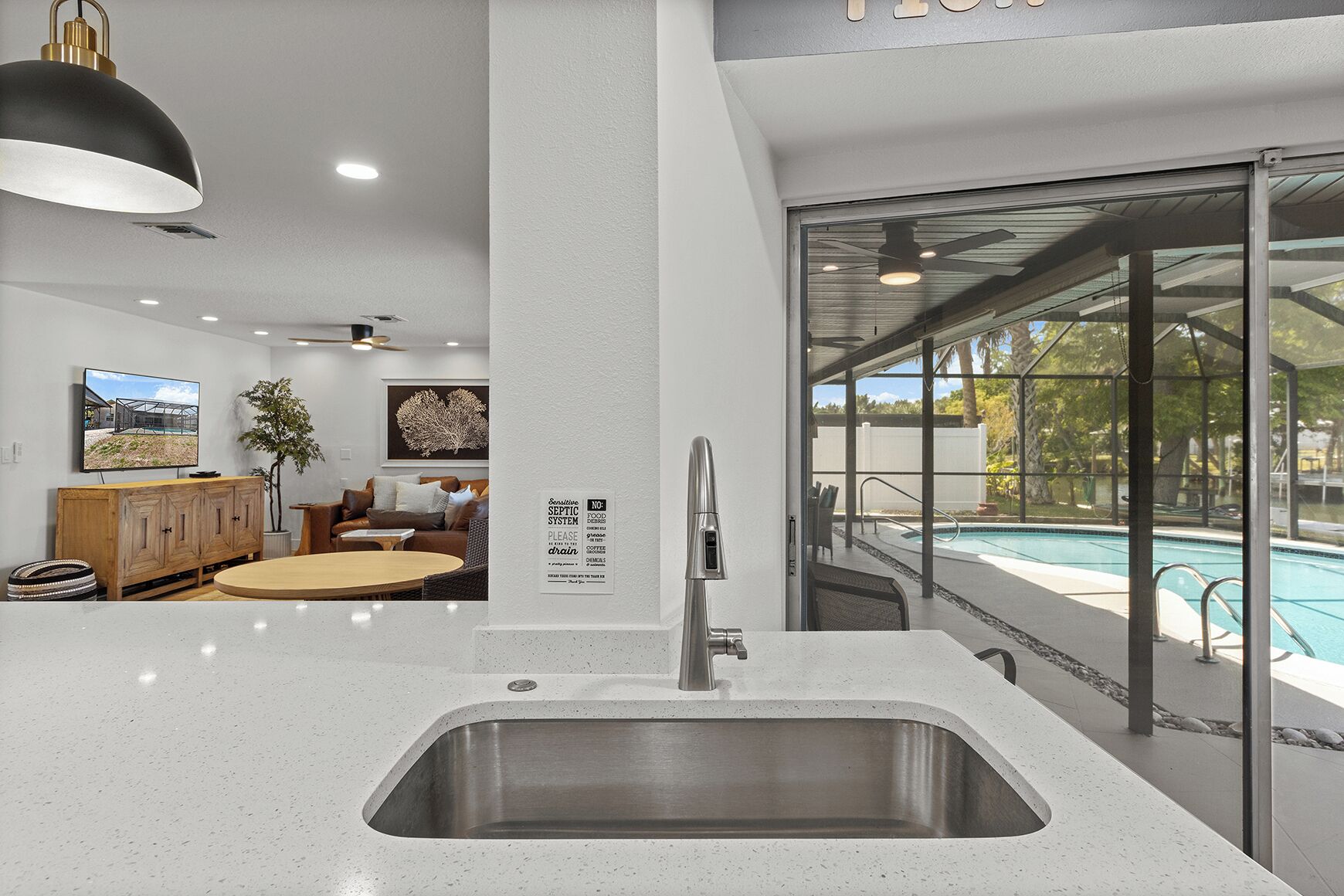 Une cuisine moderne dotée d’un évier en acier inoxydable, d’un coin repas avec une table ronde et d’une vue sur une piscine, visible à travers de grandes portes vitrées.