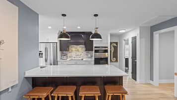 A modern kitchen with a large island, bar stools, stainless steel appliances, and pendant lighting.