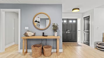 A modern hallway with a wooden console table, a mirror, wicker baskets, and a dark door.