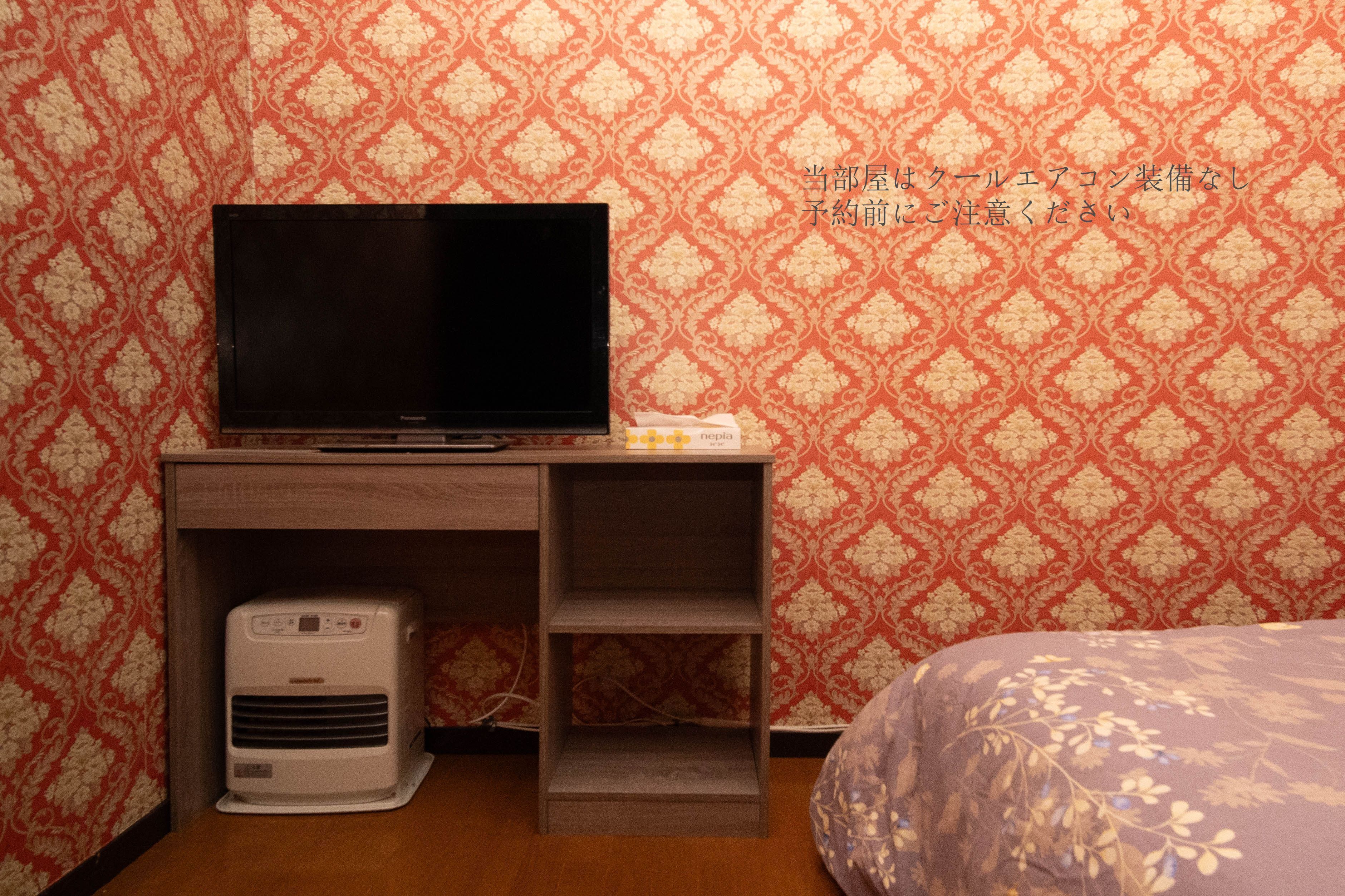 A hotel room with a television on a wooden stand, a small air conditioning unit, and a patterned wall.