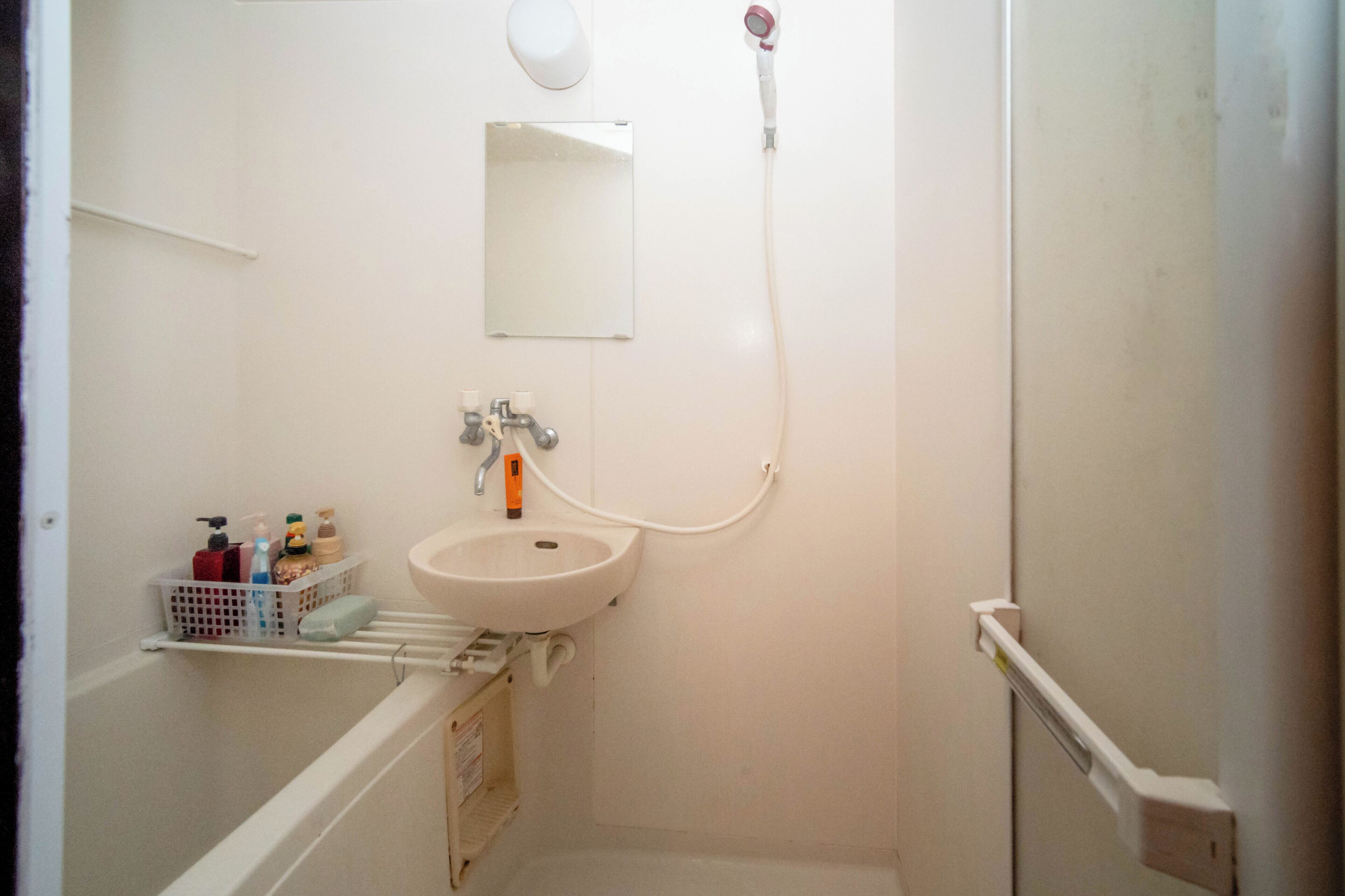 Un baño pequeño con un lavamanos blanco, un espejo y un cabezal de ducha de mano.