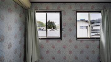 A room with floral wallpaper, two windows with curtains, and a view of houses outside.
