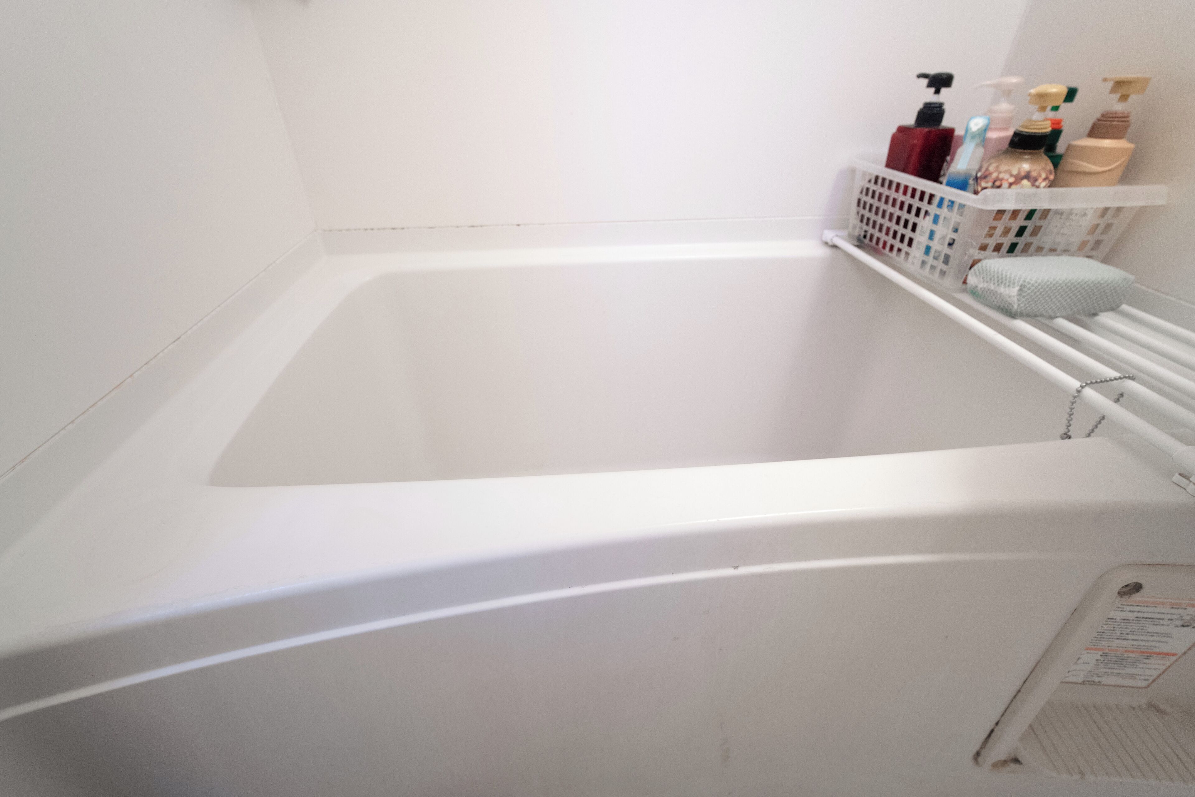 A white bathtub with a white shower curtain and a shelf with toiletries.