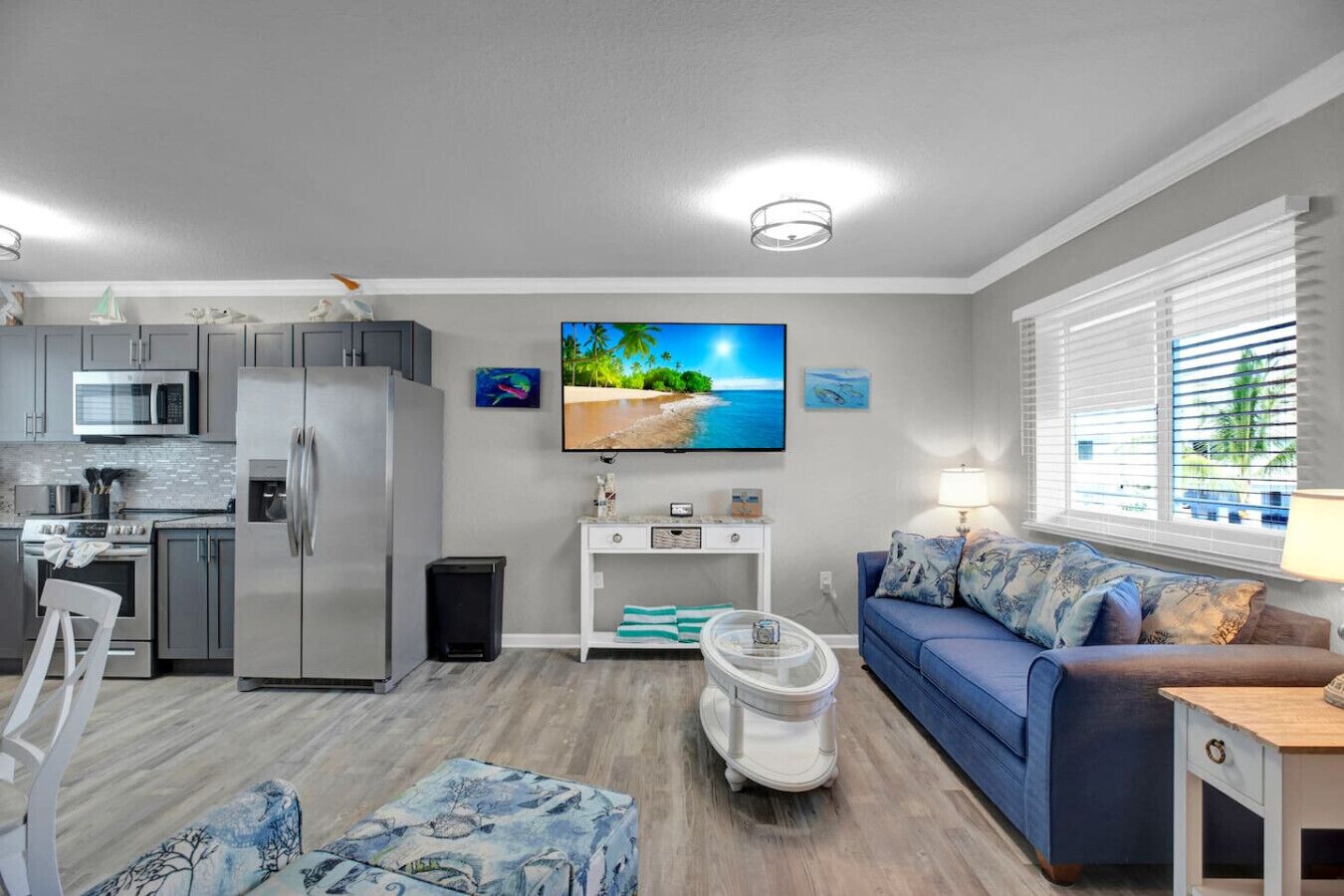 A modern living room with a blue sofa, a flat-screen TV, and a kitchen area with stainless steel appliances.