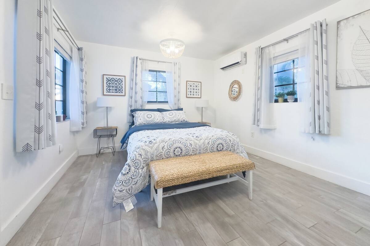A bedroom with a bed, bedside tables, a bench, and patterned curtains.
