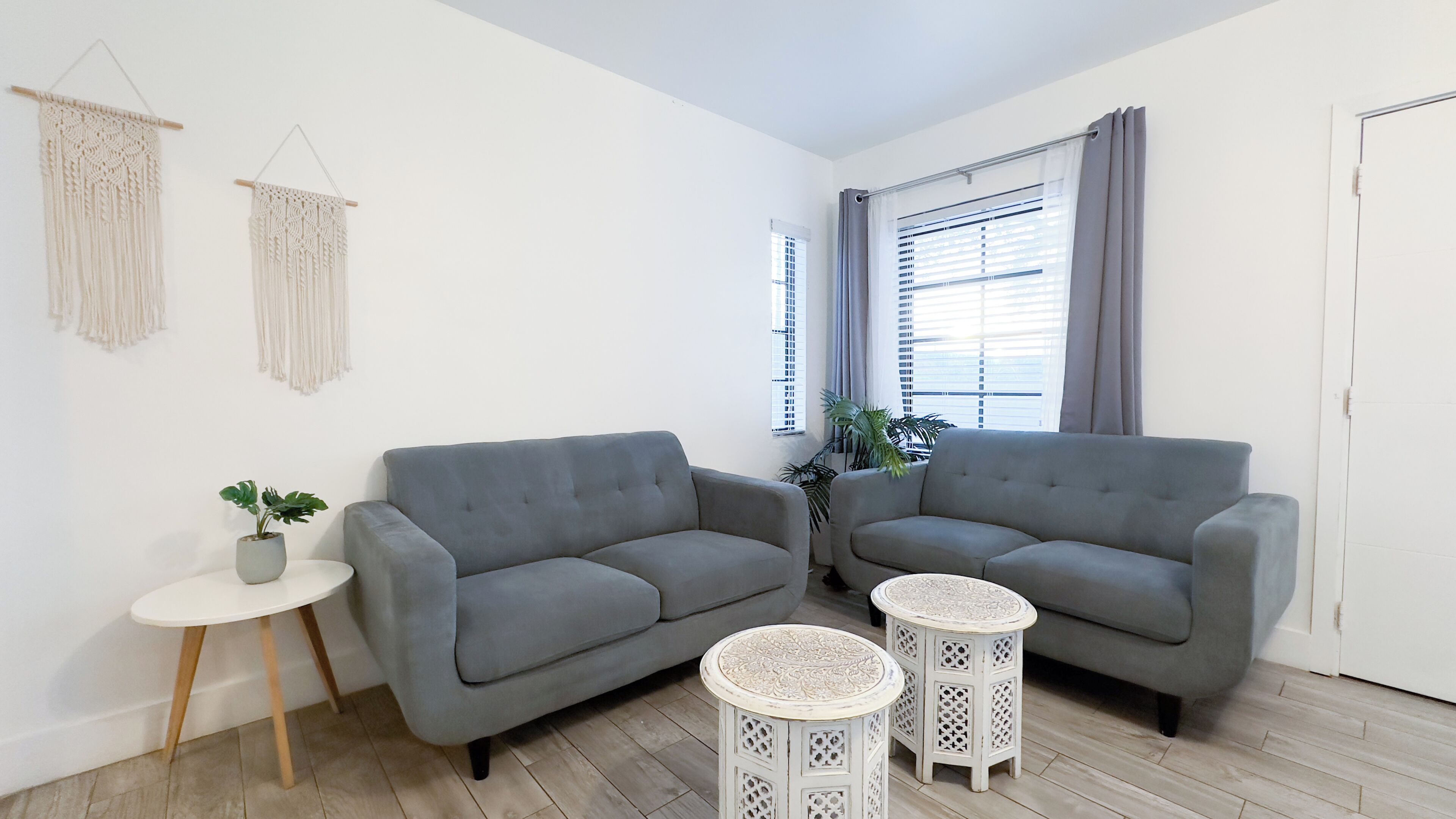 A modern living room with two grey sofas, a small white table, and two round side tables with intricate designs.