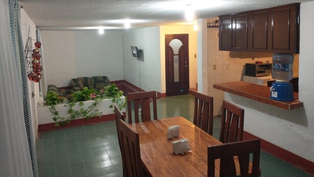 A dining area with a wooden table and chairs, a kitchen with cabinets, and a water dispenser.
