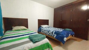 A room with two single beds, each with a wooden headboard and a patterned bedspread. There is a large wooden wardrobe against the wall.