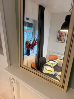 Un comedor con una mesa dispuesta para dos personas, una ventana con vistas y un espejo que refleja la habitación.