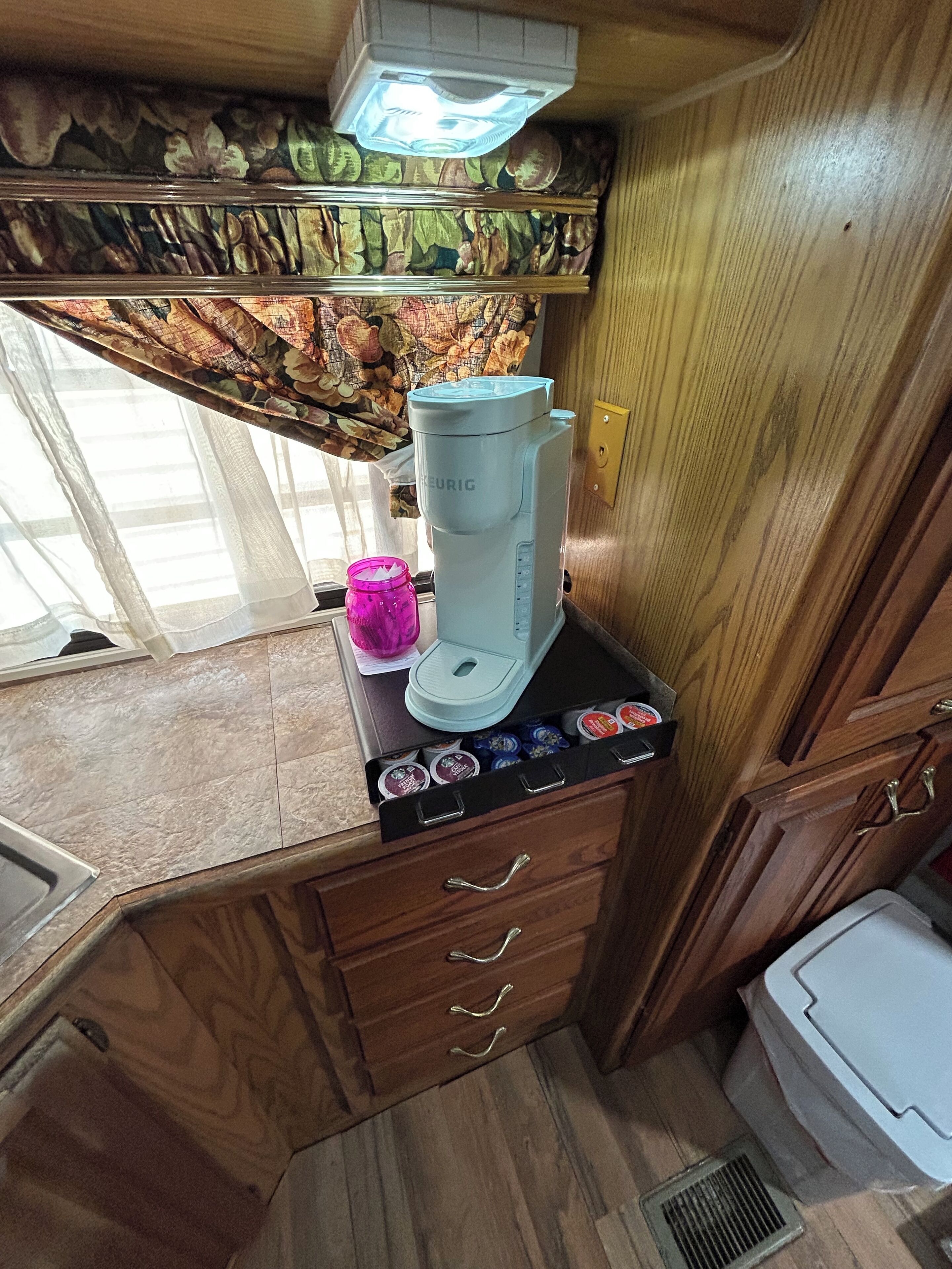 A kitchenette with a coffee maker, a jar, and a drawer unit.