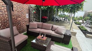 A patio area with wicker furniture, a red umbrella, and a brick wall. - Charming 1-bedroom house in adorable Elizabeth with AC, WiFi (Elizabeth)