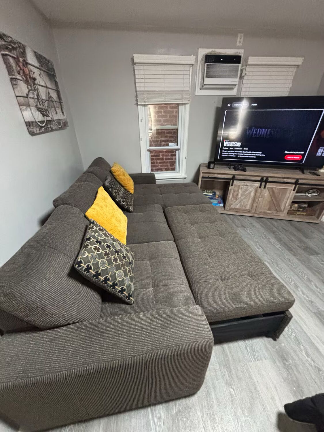 Una sala de estar con un sofá seccional, televisor y pared de ladrillo.
