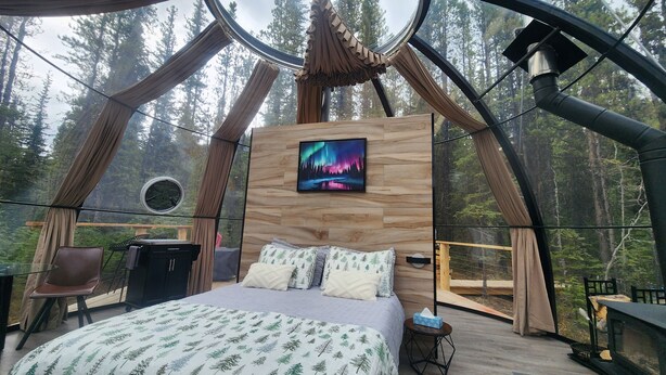 A cozy bedroom with a bed, pillows, and a TV screen displaying a forest scene.