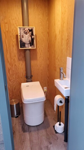 Een kleine, compacte badkamer met een houten wand, een toilet, een wastafel en een prullenbak.