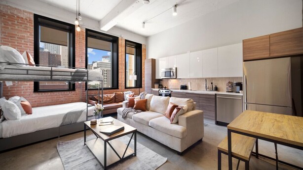Eine moderne Wohnung mit Schlafplatz im Loft-Stil, einer Couch, einem Esstisch und einer Küchenzeile.