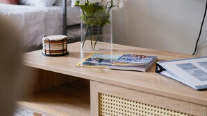 Una habitación acogedora con una cama litera, una mesa de centro de madera con un libro y un jarrón de flores, y un televisor en la pared.